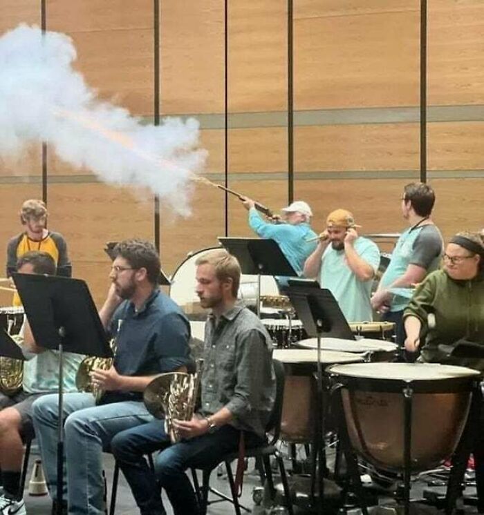 Orchestra practice scene with musicians unfazed by a man creating smoke with a long stick, capturing a 'hmmm' moment. Orchestra practice scene with musicians unfazed by a man creating smoke with a long stick, capturing a 'hmmm' moment.