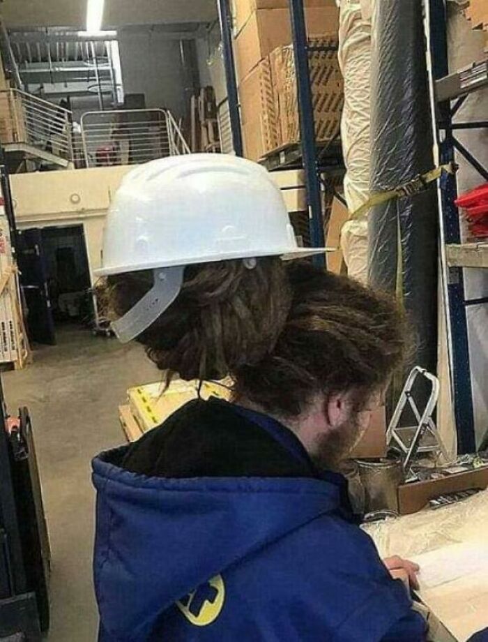 Person with a unique hard hat fit due to hairstyle in a warehouse, creating a 'hmmm' moment. Person with a unique hard hat fit due to hairstyle in a warehouse, creating a 'hmmm' moment.