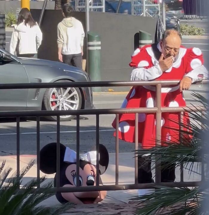 Man in polka dot dress, holding Minnie Mouse head, making people go "hmmm" on a city street. Man in polka dot dress, holding Minnie Mouse head, making people go "hmmm" on a city street.