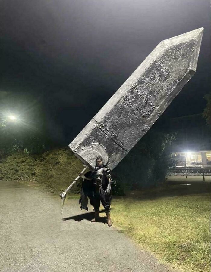 A person dressed in a costume holds an enormous sword at night, evoking curiosity. A person dressed in a costume holds an enormous sword at night, evoking curiosity.