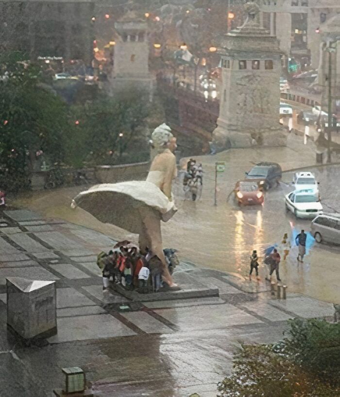 Group shelters under large statue's dress during rain, a quirky sight making them go 'hmmm'. Group shelters under large statue's dress during rain, a quirky sight making them go 'hmmm'.
